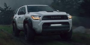 A white 2025 Toyota 4Runner navigating a rugged, muddy trail surrounded by dense trees.