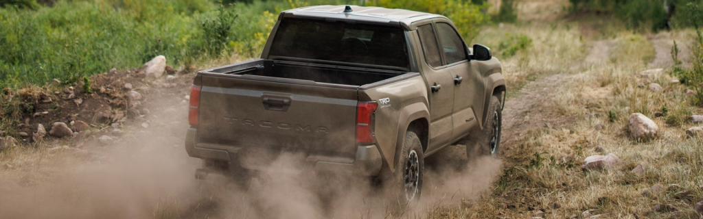 Toyota Tacoma truck driving on a dusty off-road path.