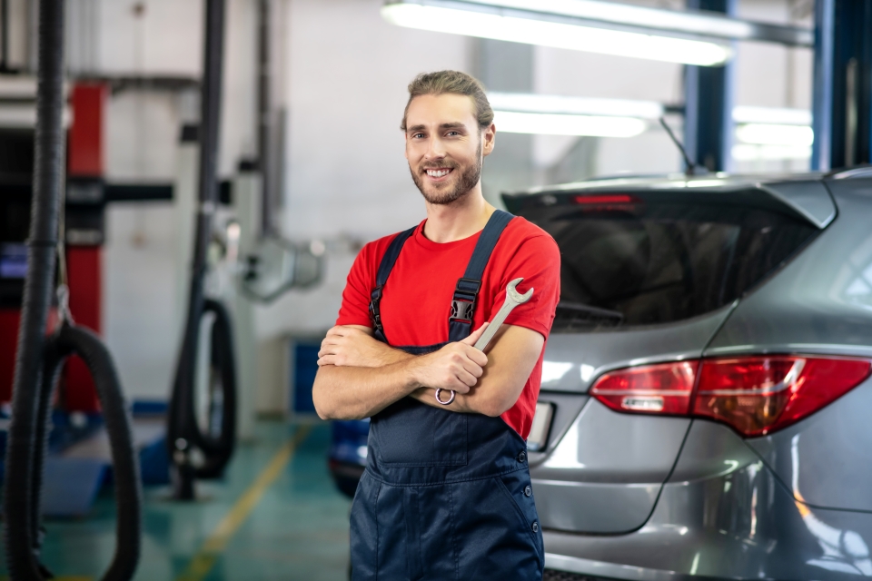 Smiling mechanic in overalls holding a wrench in an auto repair shop